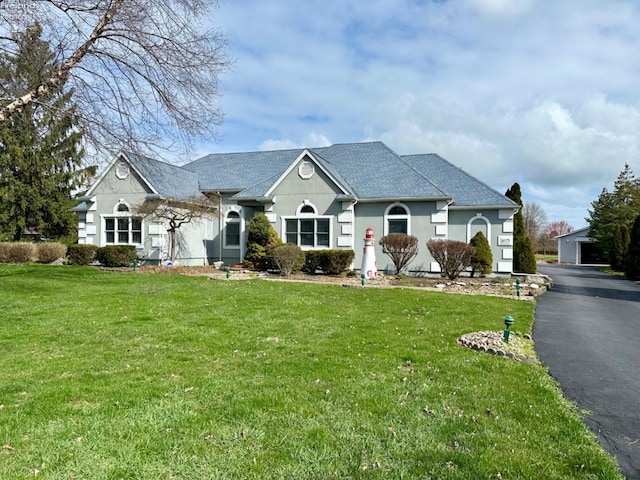 ranch-style house with aphalt driveway, roof with shingles, a front lawn, and stucco siding