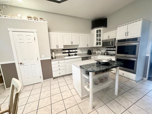 kitchen featuring light tile patterned floors, glass insert cabinets, appliances with stainless steel finishes, white cabinetry, and a sink