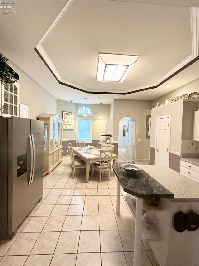 kitchen featuring arched walkways, light tile patterned flooring, a kitchen breakfast bar, stainless steel fridge with ice dispenser, and a tray ceiling