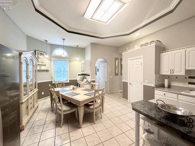 dining space featuring arched walkways, light tile patterned floors, a raised ceiling, and ornamental molding