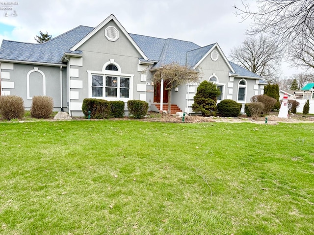 view of front of house featuring roof with shingles, a front lawn, and stucco siding