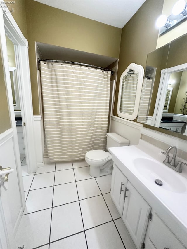 bathroom featuring a shower with shower curtain, toilet, a wainscoted wall, tile patterned flooring, and vanity