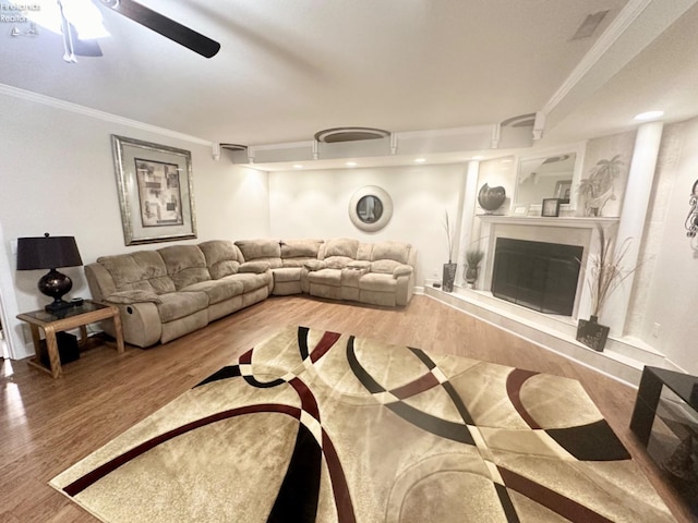 living room with a ceiling fan, ornamental molding, wood finished floors, and a glass covered fireplace