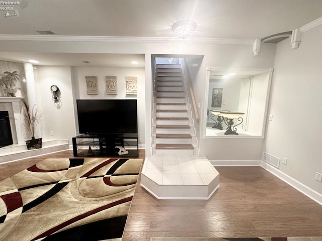 living room with wood finished floors, baseboards, stairs, ornamental molding, and a tiled fireplace