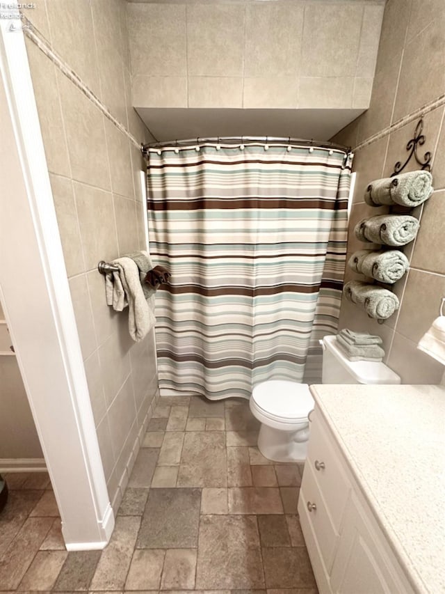 full bathroom with curtained shower, toilet, stone tile floors, vanity, and tile walls