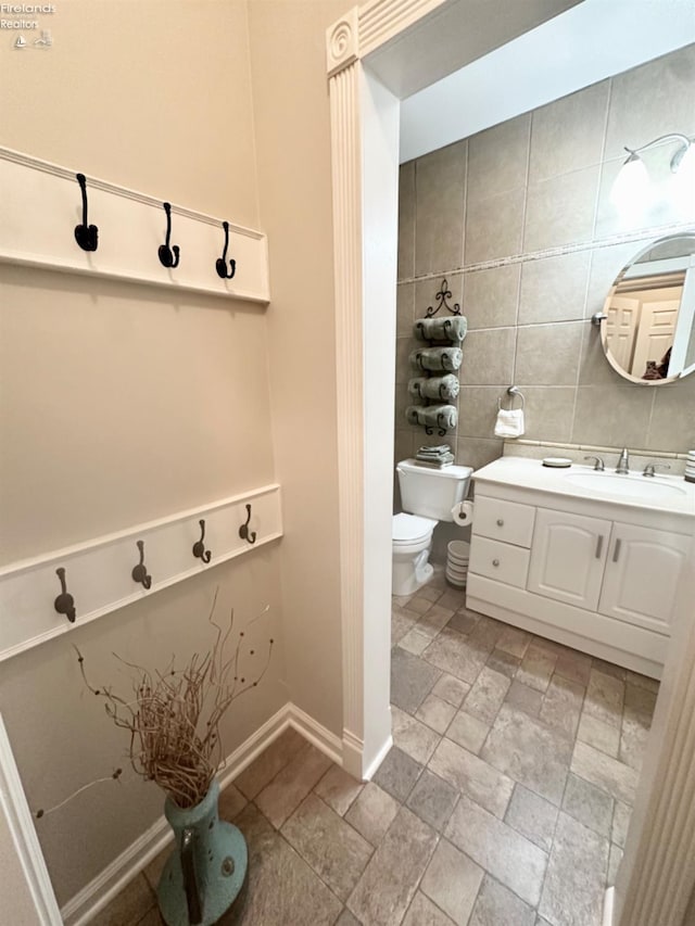 bathroom featuring toilet, baseboards, tile walls, and vanity