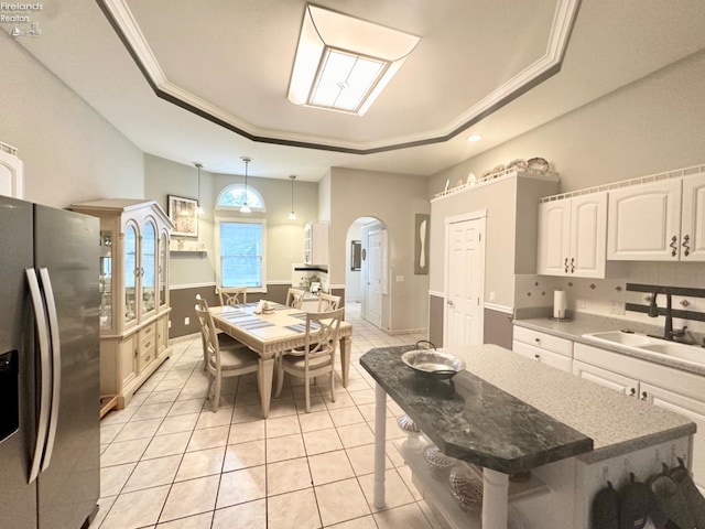 kitchen with arched walkways, white cabinets, stainless steel fridge with ice dispenser, a tray ceiling, and a sink