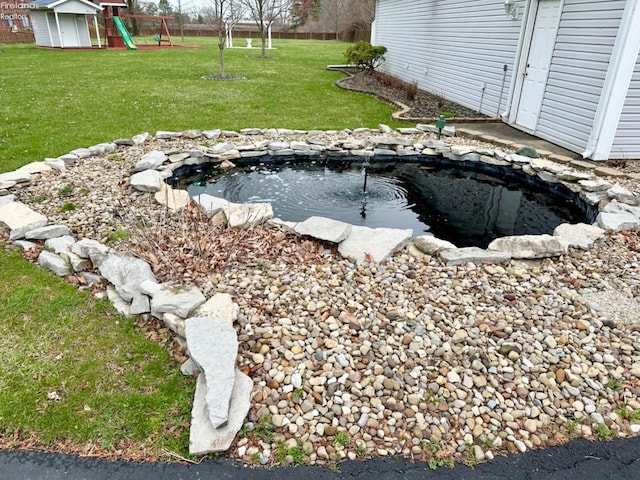 exterior space featuring an outbuilding, a playground, and a small pond