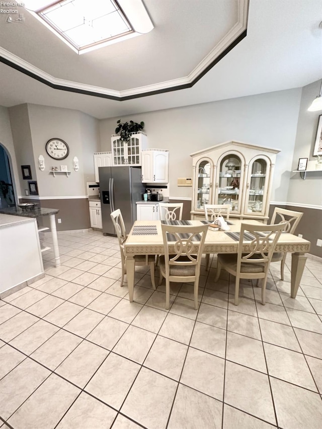 dining area with light tile patterned floors, a tray ceiling, and arched walkways