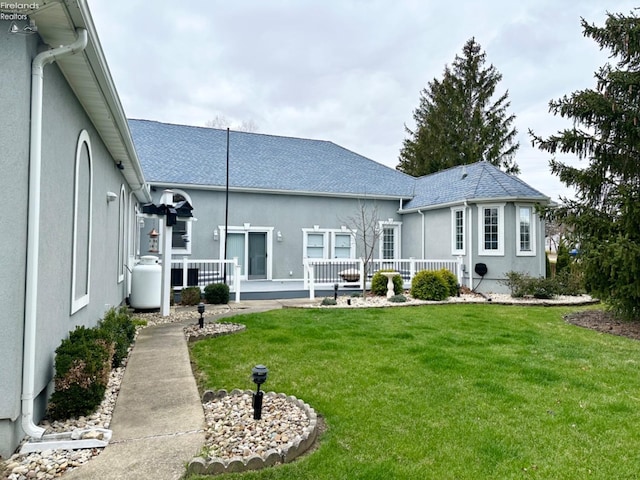 rear view of property featuring a shingled roof, a lawn, and stucco siding