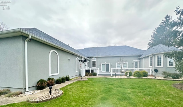 back of property featuring a shingled roof, a lawn, and stucco siding