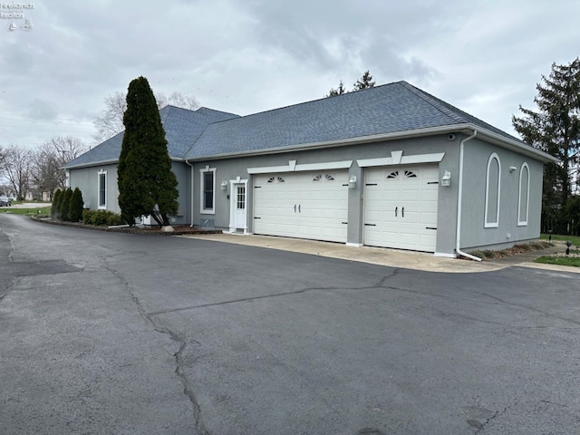 ranch-style home featuring roof with shingles, an attached garage, and stucco siding