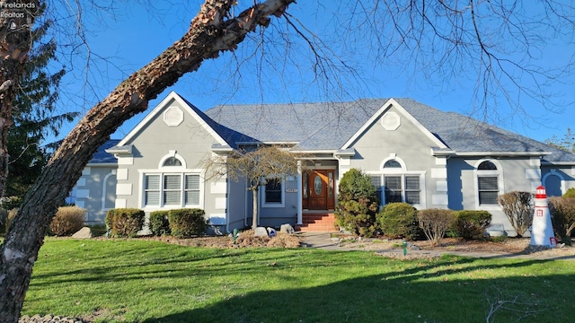 view of front of property with roof with shingles, a front yard, and stucco siding