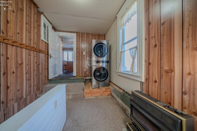 washroom featuring wooden walls, heating unit, carpet, laundry area, and stacked washer and clothes dryer