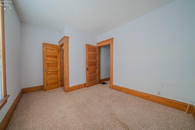 unfurnished bedroom with a textured ceiling, light colored carpet, visible vents, and baseboards