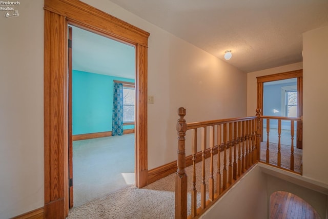 hall featuring baseboards, an upstairs landing, and carpet floors