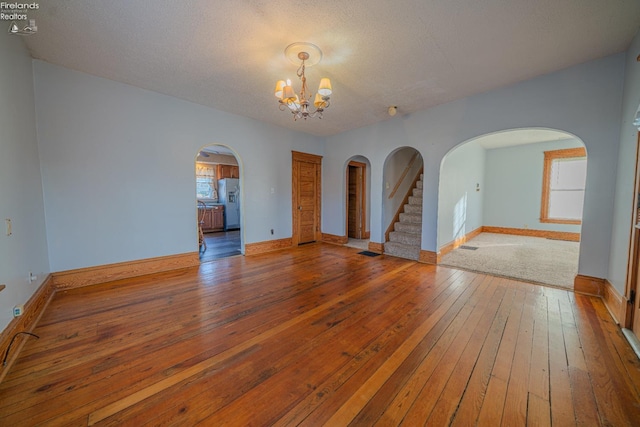 unfurnished room with hardwood / wood-style floors, stairway, baseboards, and a chandelier