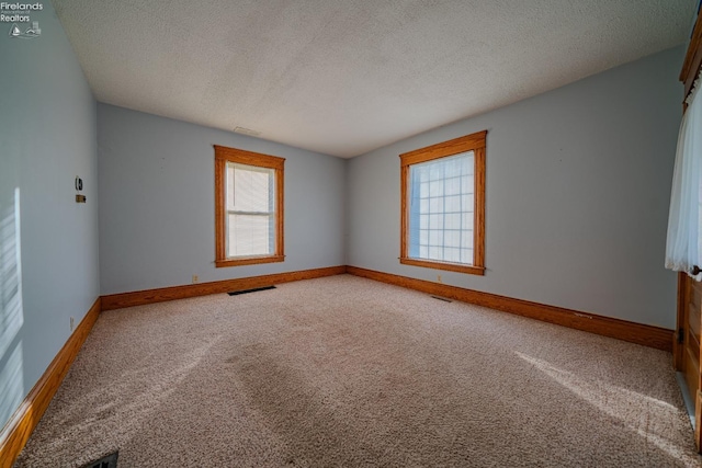 spare room with carpet flooring, a healthy amount of sunlight, visible vents, and baseboards