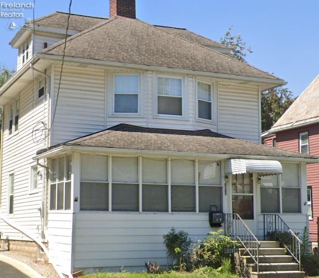 traditional style home featuring a shingled roof, a chimney, and a sunroom