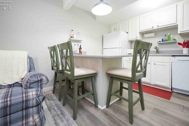 kitchen with light wood-style floors, white appliances, light countertops, and a kitchen bar