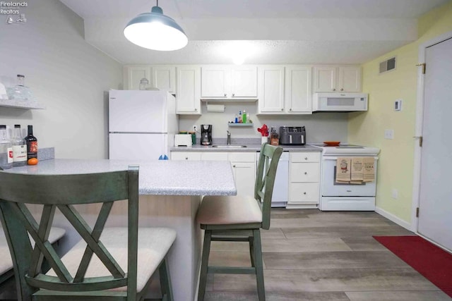 kitchen featuring white appliances, visible vents, white cabinets, a kitchen bar, and a sink