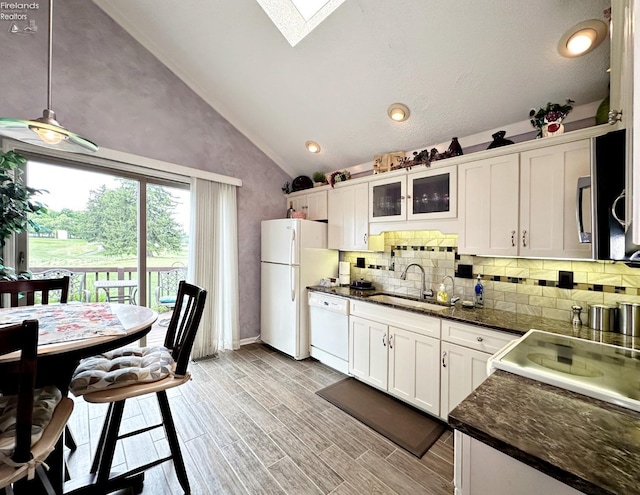 kitchen with vaulted ceiling with skylight, white appliances, a sink, white cabinets, and light wood-style floors