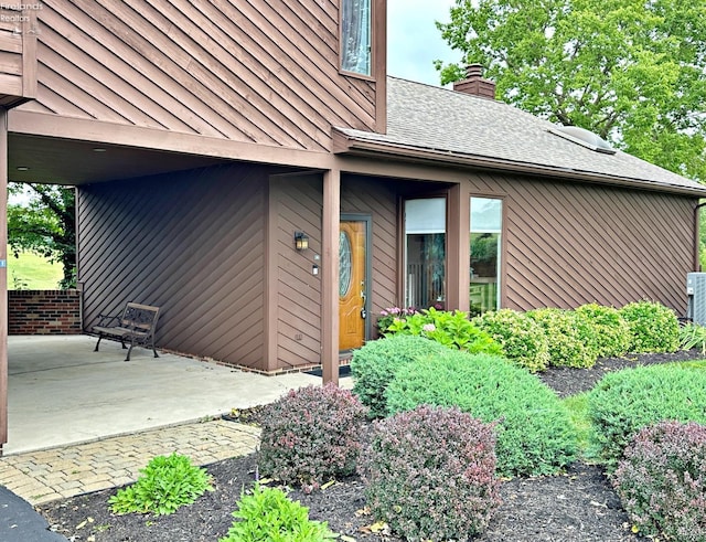 entrance to property with a standing seam roof, metal roof, roof with shingles, a chimney, and a patio area