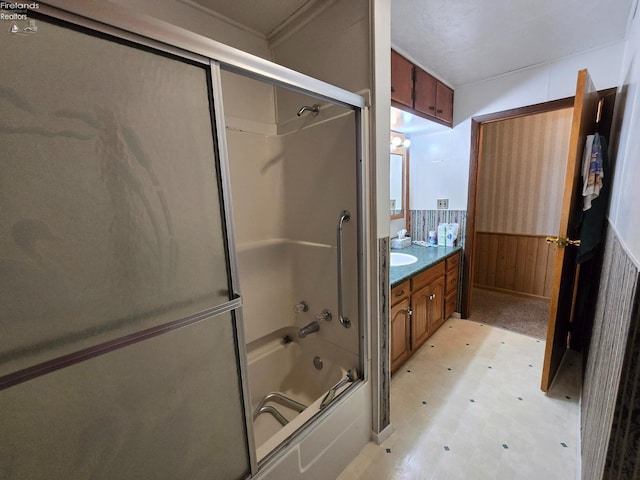 full bath featuring a wainscoted wall, shower / bath combination with glass door, wood walls, vanity, and tile patterned floors