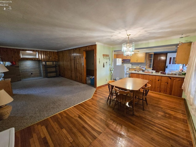 dining room featuring wood walls, crown molding, a chandelier, and wood finished floors