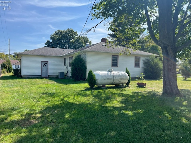 back of property with central AC, a yard, and a chimney