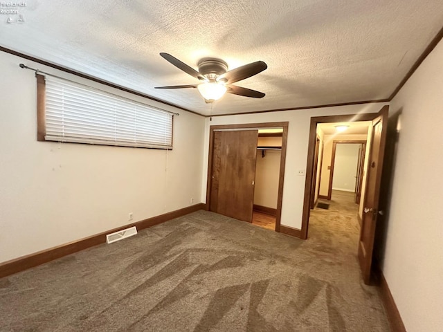 unfurnished bedroom with a textured ceiling, visible vents, carpet floors, baseboards, and a closet