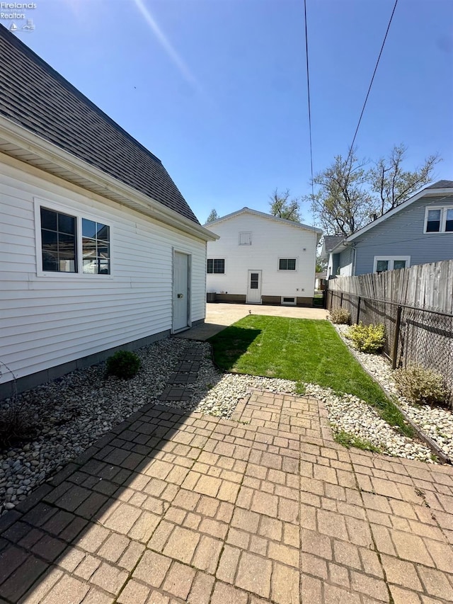 rear view of house with fence, a shingled roof, a yard, and a patio area