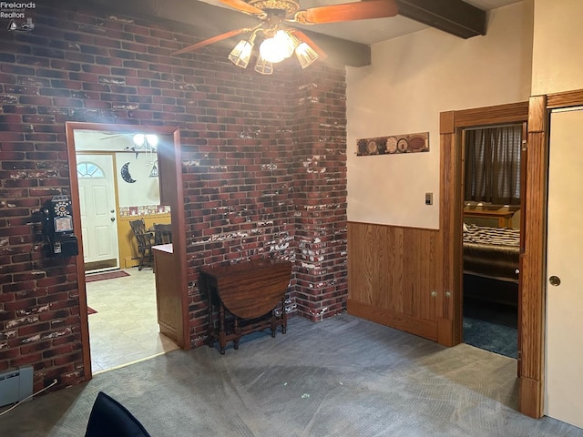 interior space with beam ceiling, wainscoting, wood walls, ceiling fan, and brick wall