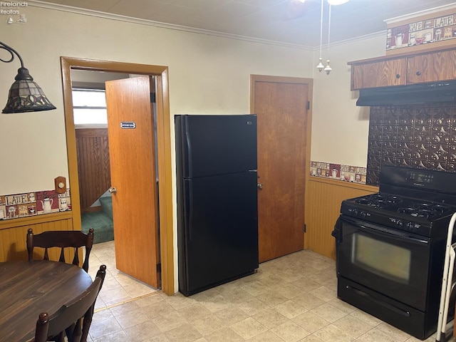 kitchen featuring a wainscoted wall, ornamental molding, wooden walls, under cabinet range hood, and black appliances