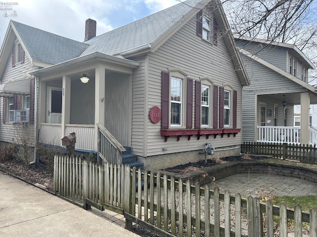 view of front of property featuring a chimney, fence, a porch, and roof with shingles