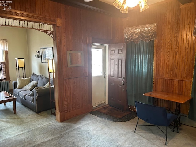 entrance foyer with arched walkways, wood walls, carpet flooring, and radiator