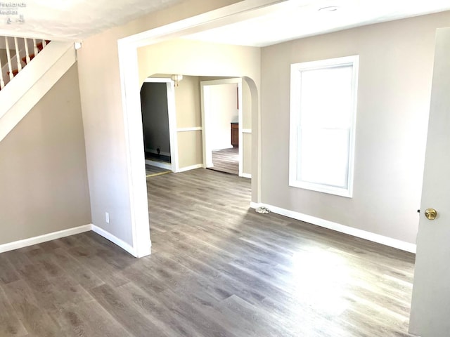 unfurnished room with baseboards, arched walkways, wood finished floors, and stairway