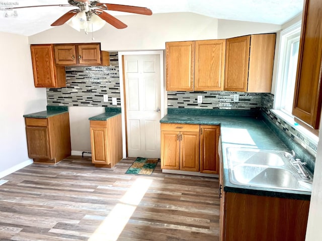 kitchen featuring lofted ceiling, decorative backsplash, brown cabinets, light wood-style flooring, and a sink