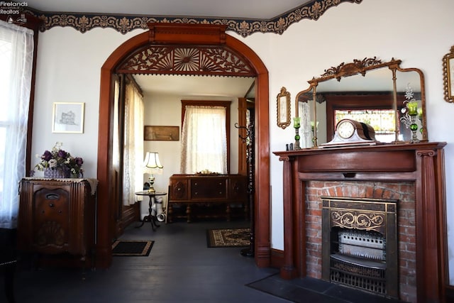 interior space featuring arched walkways, plenty of natural light, a brick fireplace, and wood finished floors