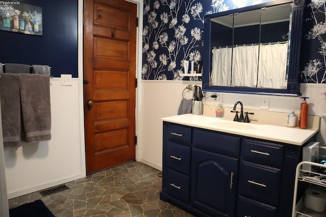 full bath with a wainscoted wall, wallpapered walls, vanity, and visible vents