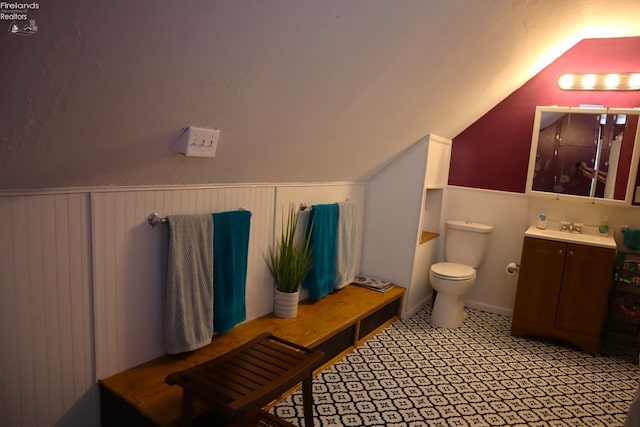 bathroom with a wainscoted wall, lofted ceiling, toilet, and vanity