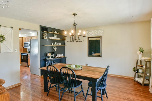 dining area featuring a barn door, a notable chandelier, light wood-style floors, and baseboards