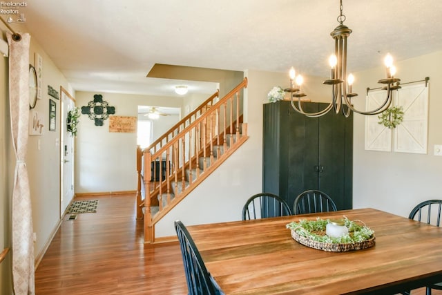 dining area featuring baseboards, wood finished floors, stairs, and ceiling fan with notable chandelier