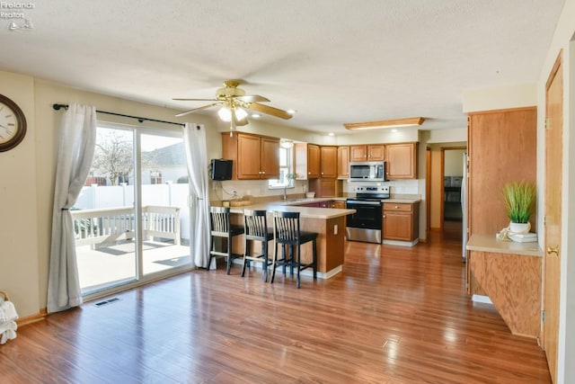 kitchen featuring wood finished floors, a peninsula, ceiling fan, light countertops, and appliances with stainless steel finishes