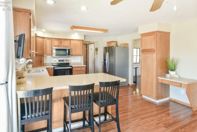 kitchen featuring a sink, light wood-style floors, appliances with stainless steel finishes, a peninsula, and light countertops