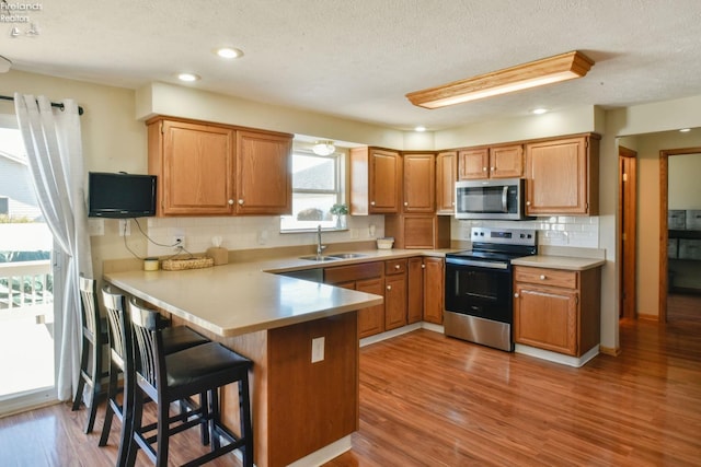 kitchen featuring light wood-style flooring, a sink, appliances with stainless steel finishes, a peninsula, and light countertops