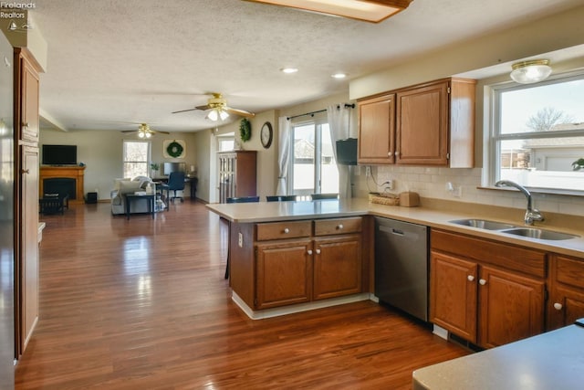 kitchen featuring a sink, backsplash, dark wood-style floors, a peninsula, and dishwasher