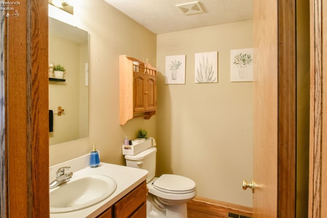 half bathroom with visible vents, toilet, a textured ceiling, wood finished floors, and vanity