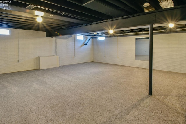 below grade area featuring a wealth of natural light, carpet flooring, and brick wall