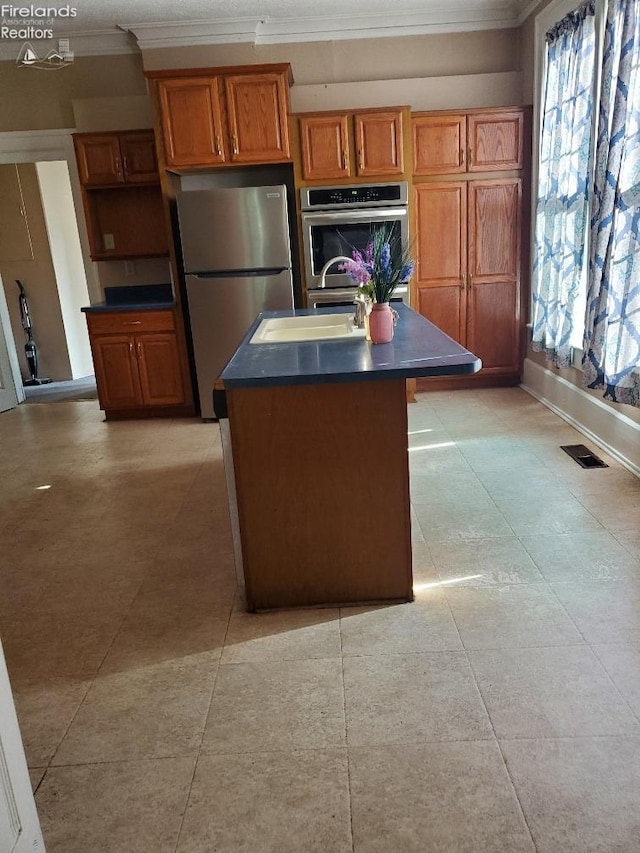 kitchen with brown cabinetry, visible vents, freestanding refrigerator, a sink, and dark countertops